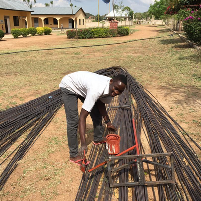 A staff member in the metal shop paints a metal stand to prevent rust.  The Lake Victoria Disability Centre Campus consisted of many yellow buildings with corrugated metal roofs, all built and maintained by LVDC staff.  Lake Victoria Disability Centre | Musoma, Tanzania.
